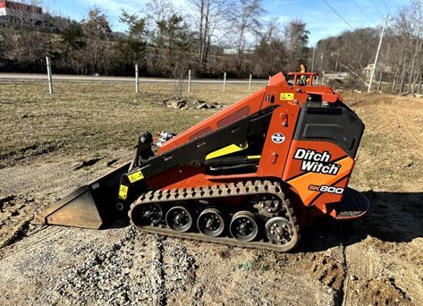 A ditch witch skid steer is sitting on top of a dirt field.