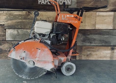 A concrete saw is sitting in front of a wooden wall.