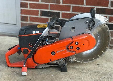 A concrete saw is sitting in front of a brick wall.