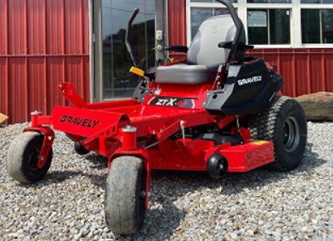 A gravely zero turn lawn mower is parked in front of a building