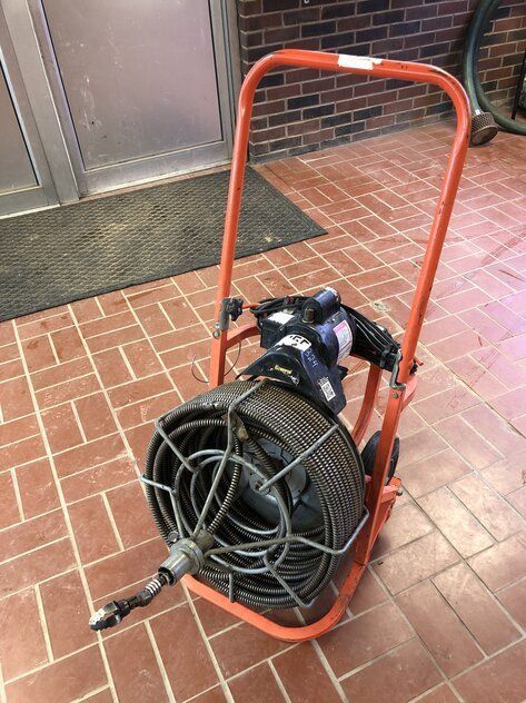 A drain cleaner is sitting on a cart on a brick floor.