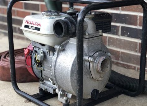 A honda water pump is sitting on the ground in front of a brick wall.