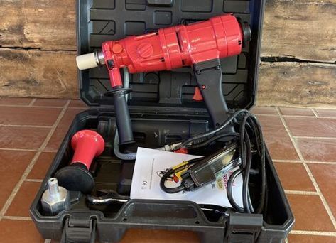 A red drill is in a black case on a tiled floor.