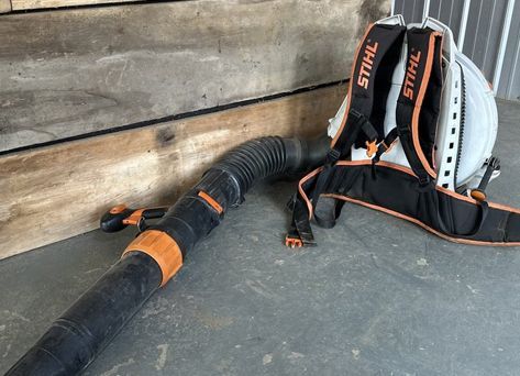 A stihl backpack blower is sitting on the ground next to a wooden wall.