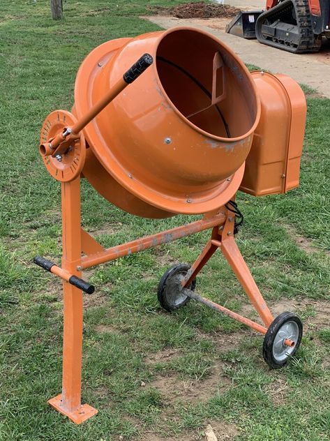 An orange concrete mixer is sitting in the grass