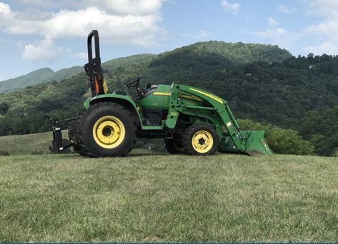 A green tractor is parked in a grassy field with mountains in the background.