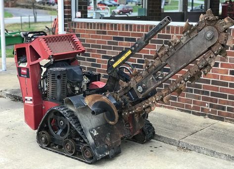 A tractor with a chainsaw attached to it is parked in front of a brick building.