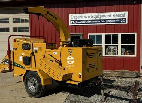 A yellow wood chipper is parked in front of a red building.