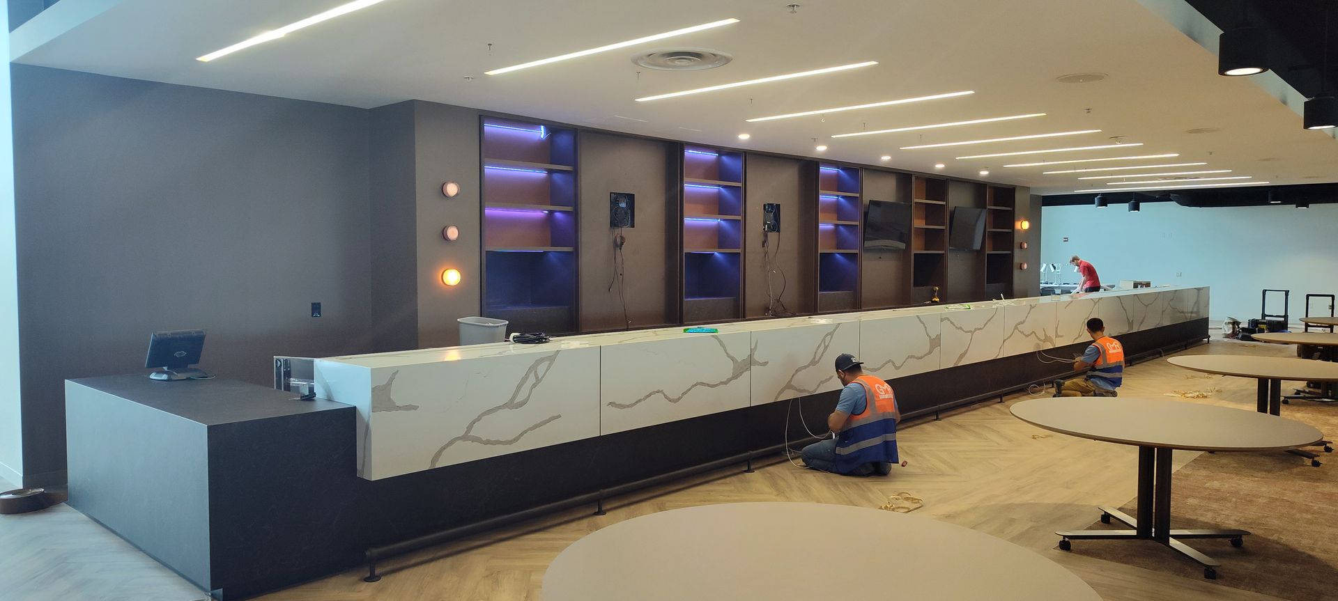 A man is kneeling on the floor in front of a long counter in a large room.