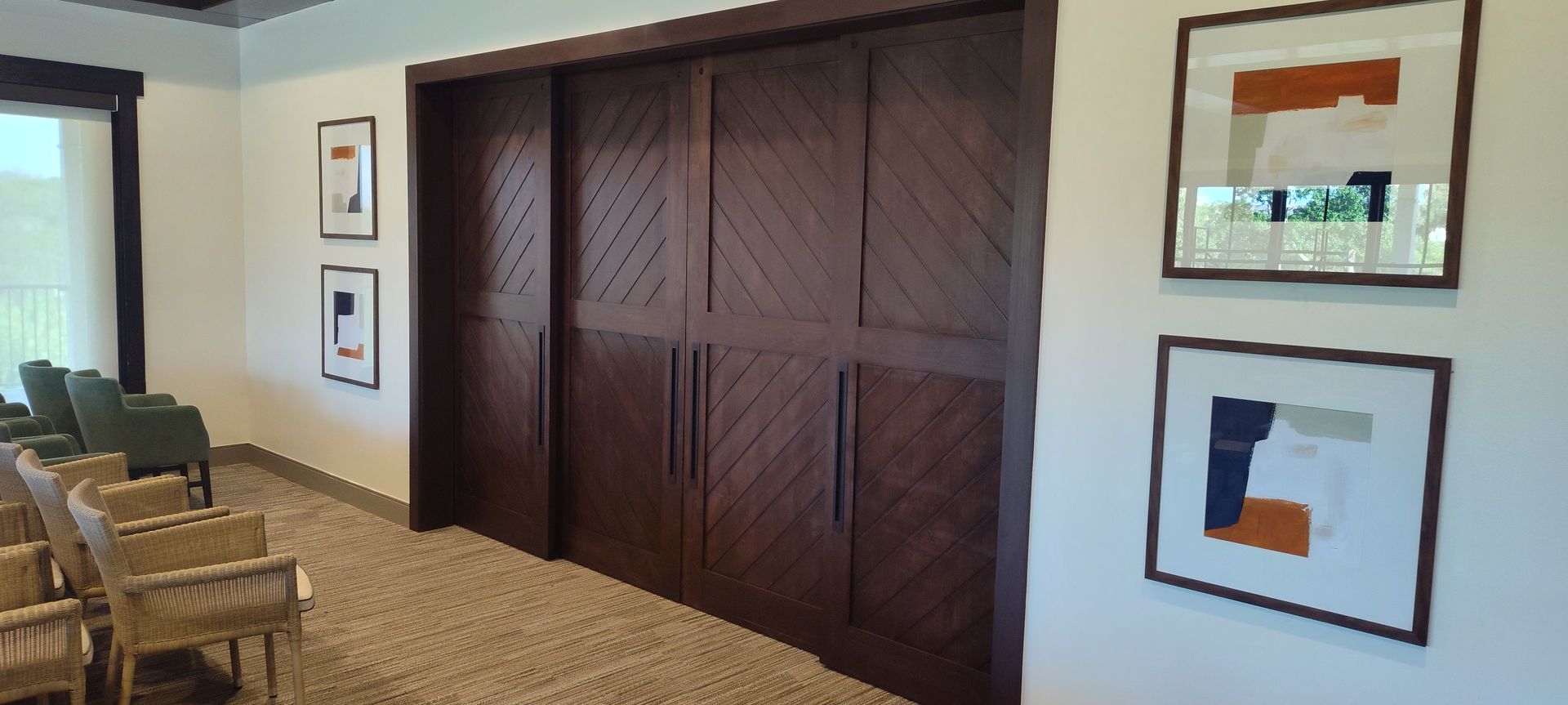 A hallway with sliding barn doors, chairs, and paintings on the wall.