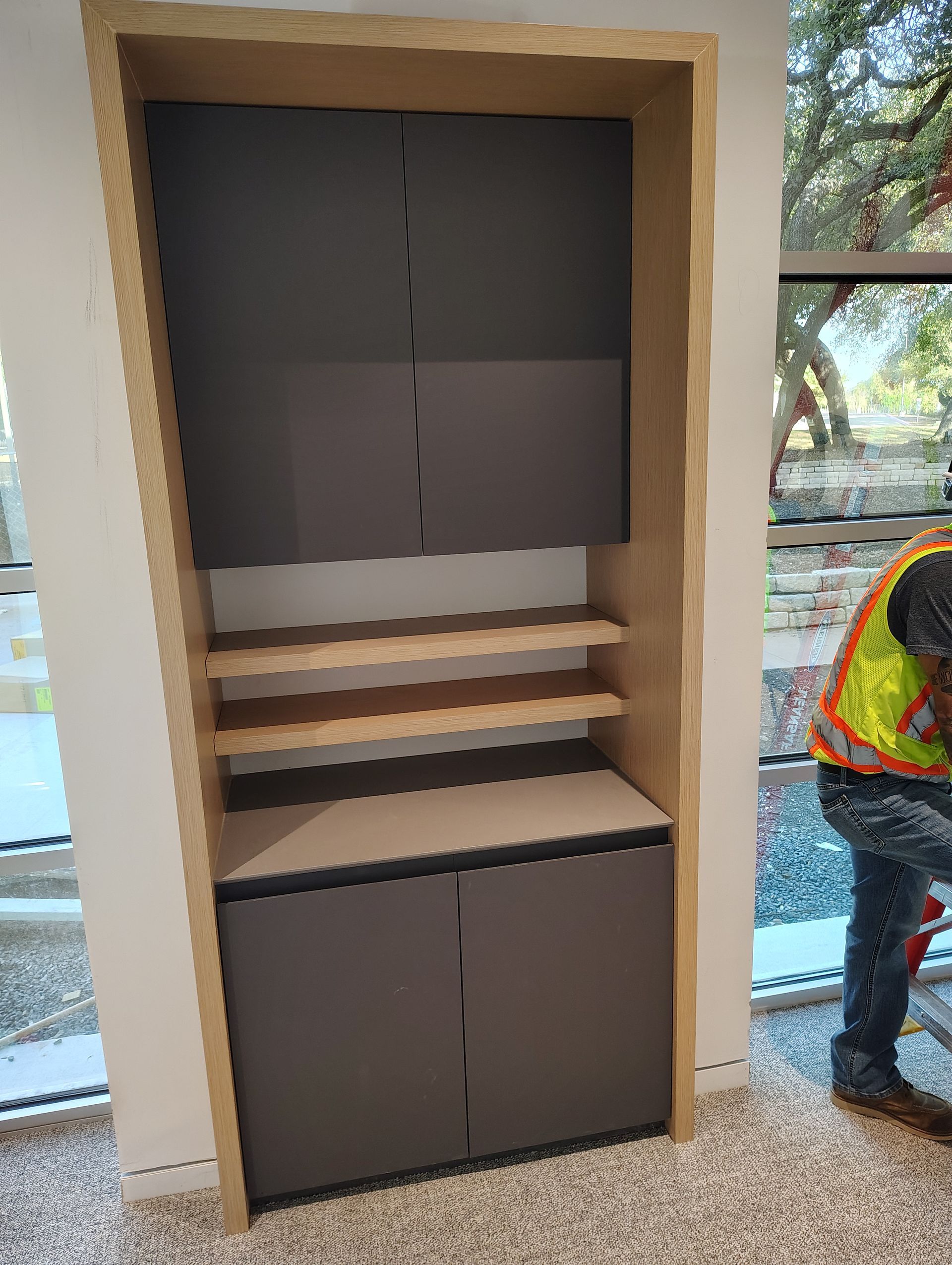 A man in a yellow vest is working on a cabinet in a room.