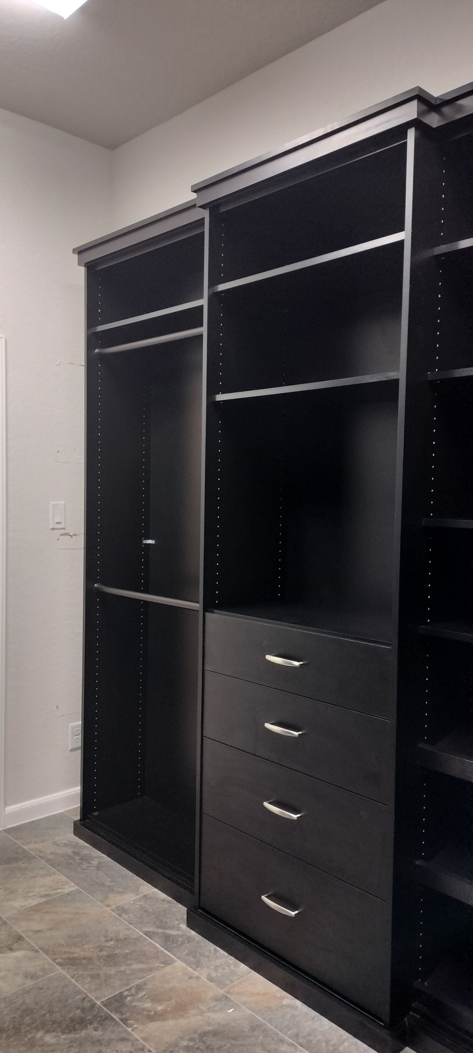 A walk in closet with lots of black shelves and drawers.