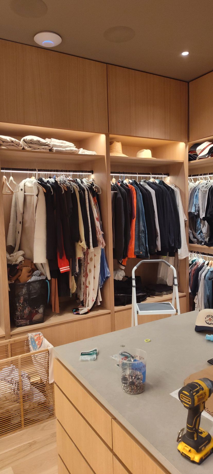 A walk in closet with lots of clothes and a drill on the counter.