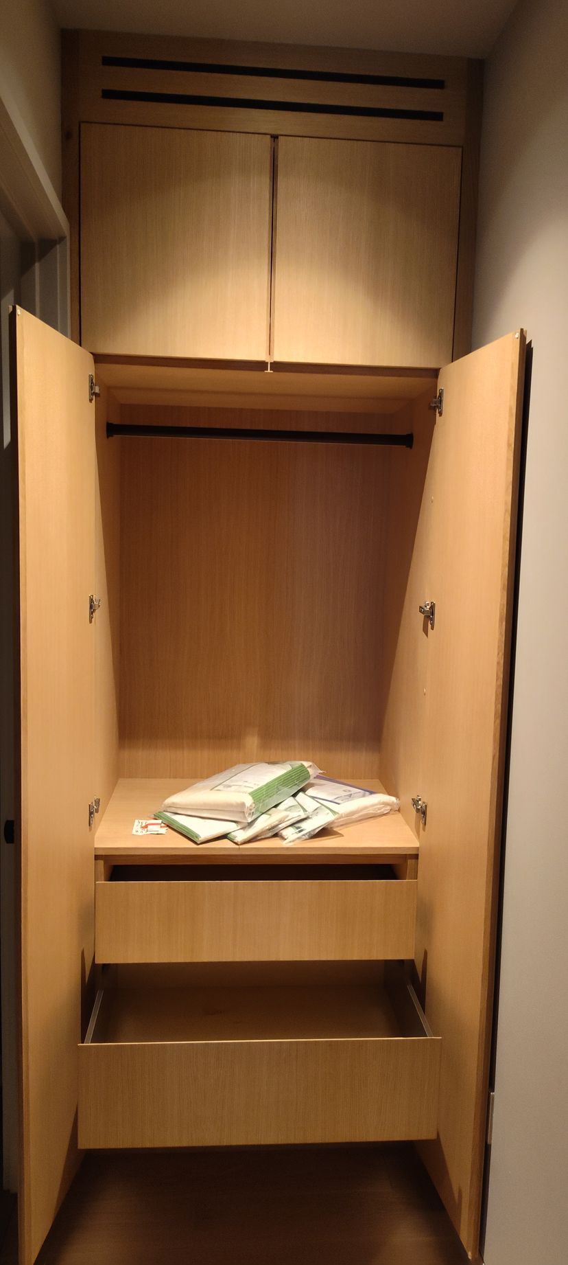 A wooden closet with the doors open and a drawer.