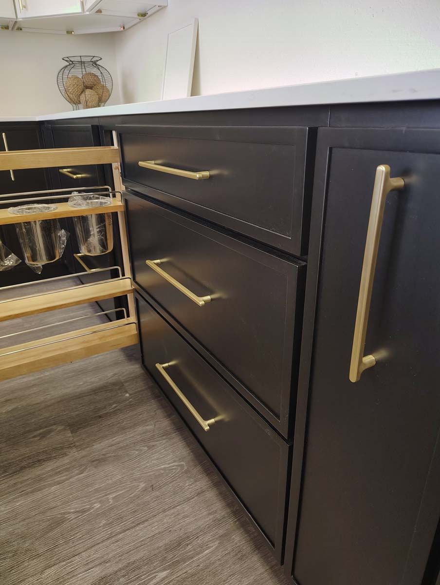 A kitchen with black cabinets and gold handles and drawers.
