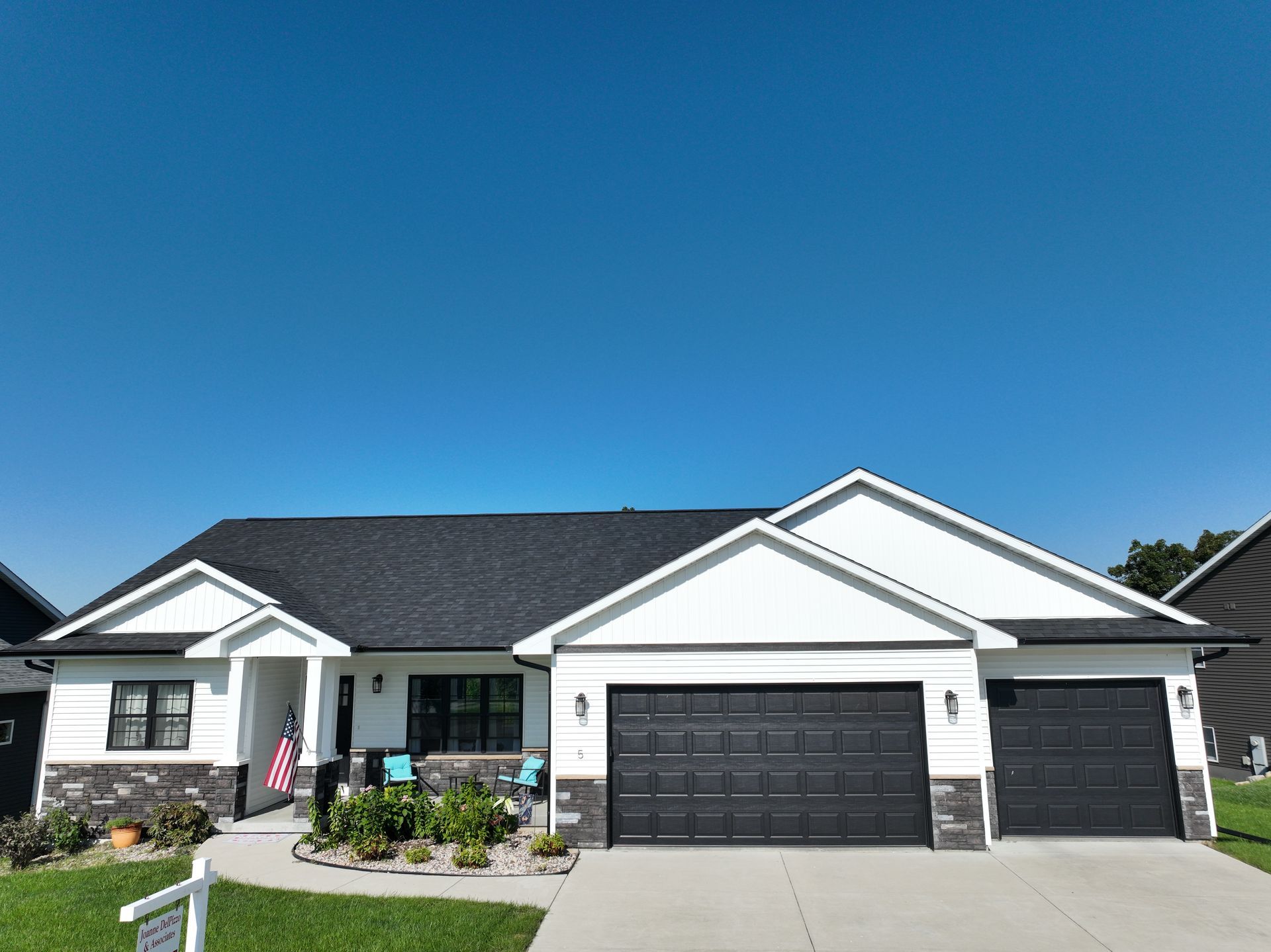 A single-story white house with a black roof, dark garage doors, stone accents, and a blue sky overhead.