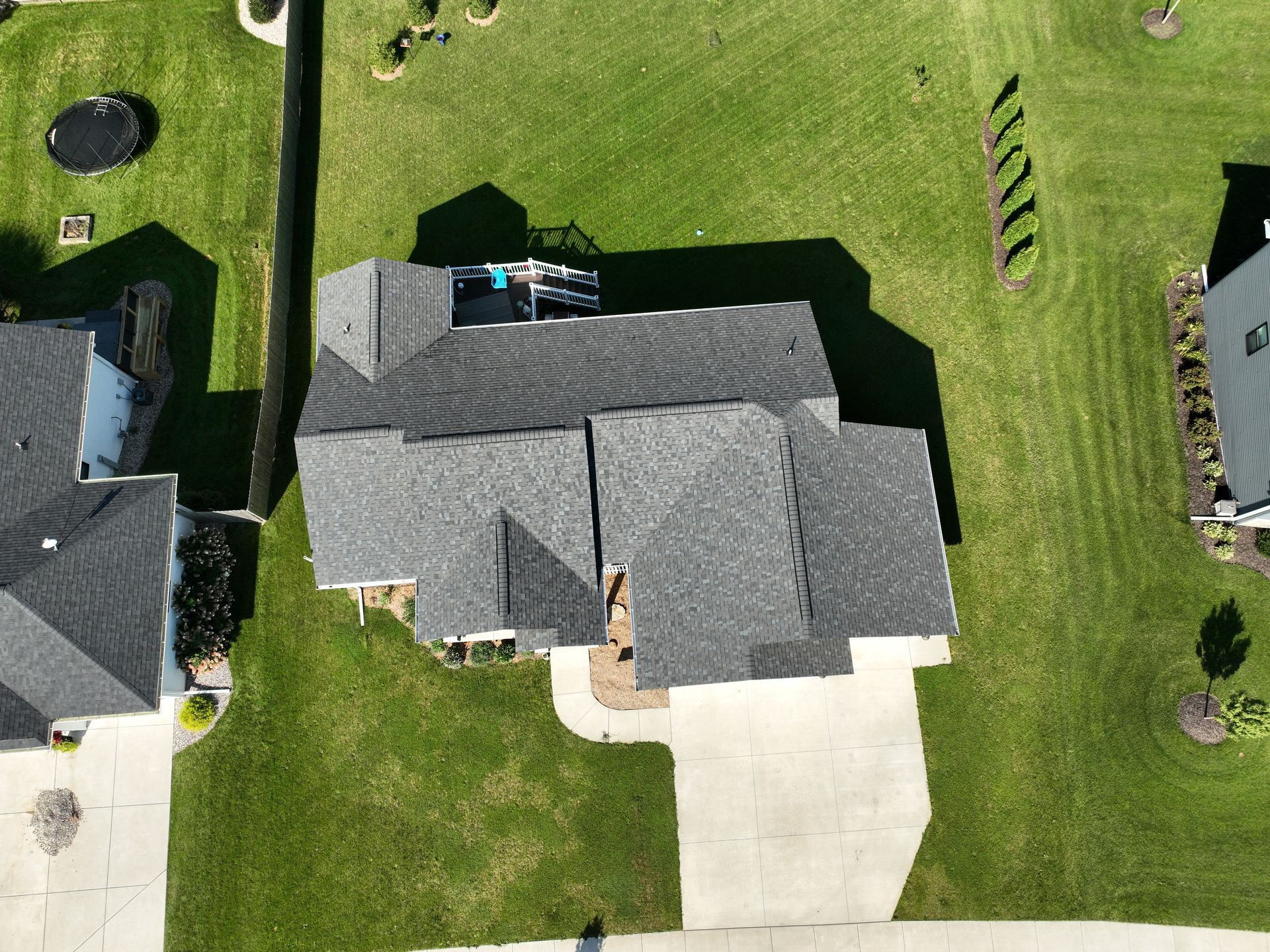 An aerial drone view of a gray-roofed residential house situated on a green lawn with a driveway and adjacent yards.