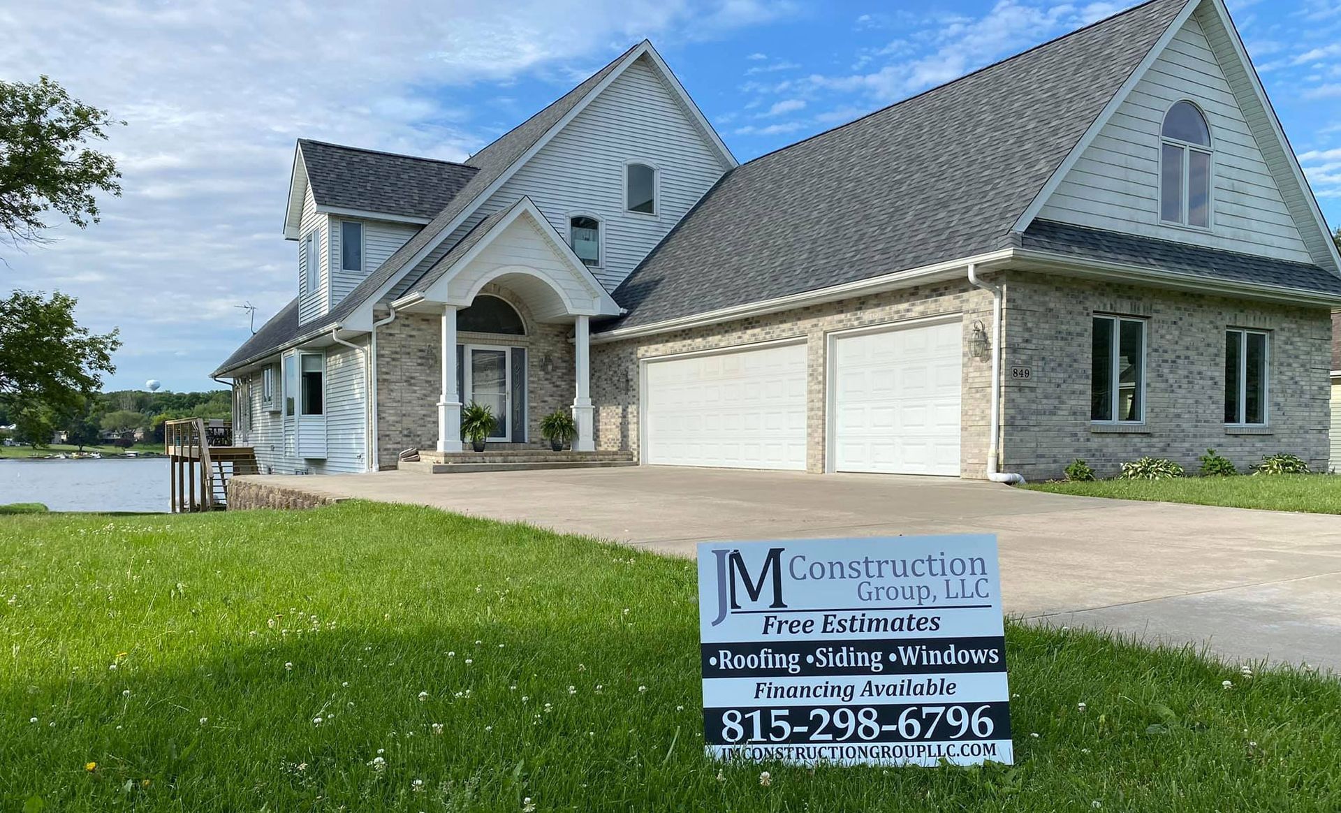 A two-story house with gray brick and roof. A JM Construction sign sits in the front yard.