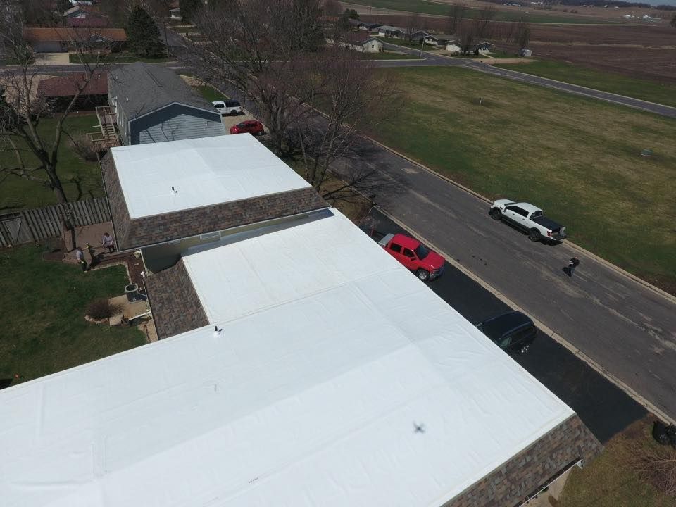 Aerial view of buildings with white roofs, a road with cars, and trees.