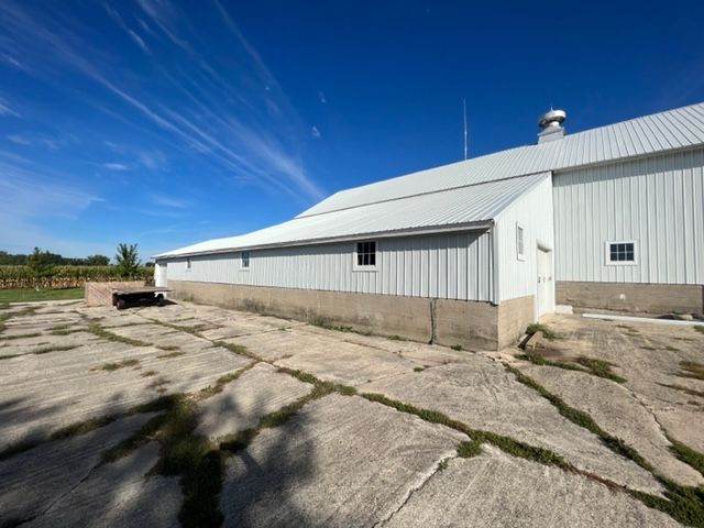 White barn with metal roof and foundation, blue sky, cracked concrete.
