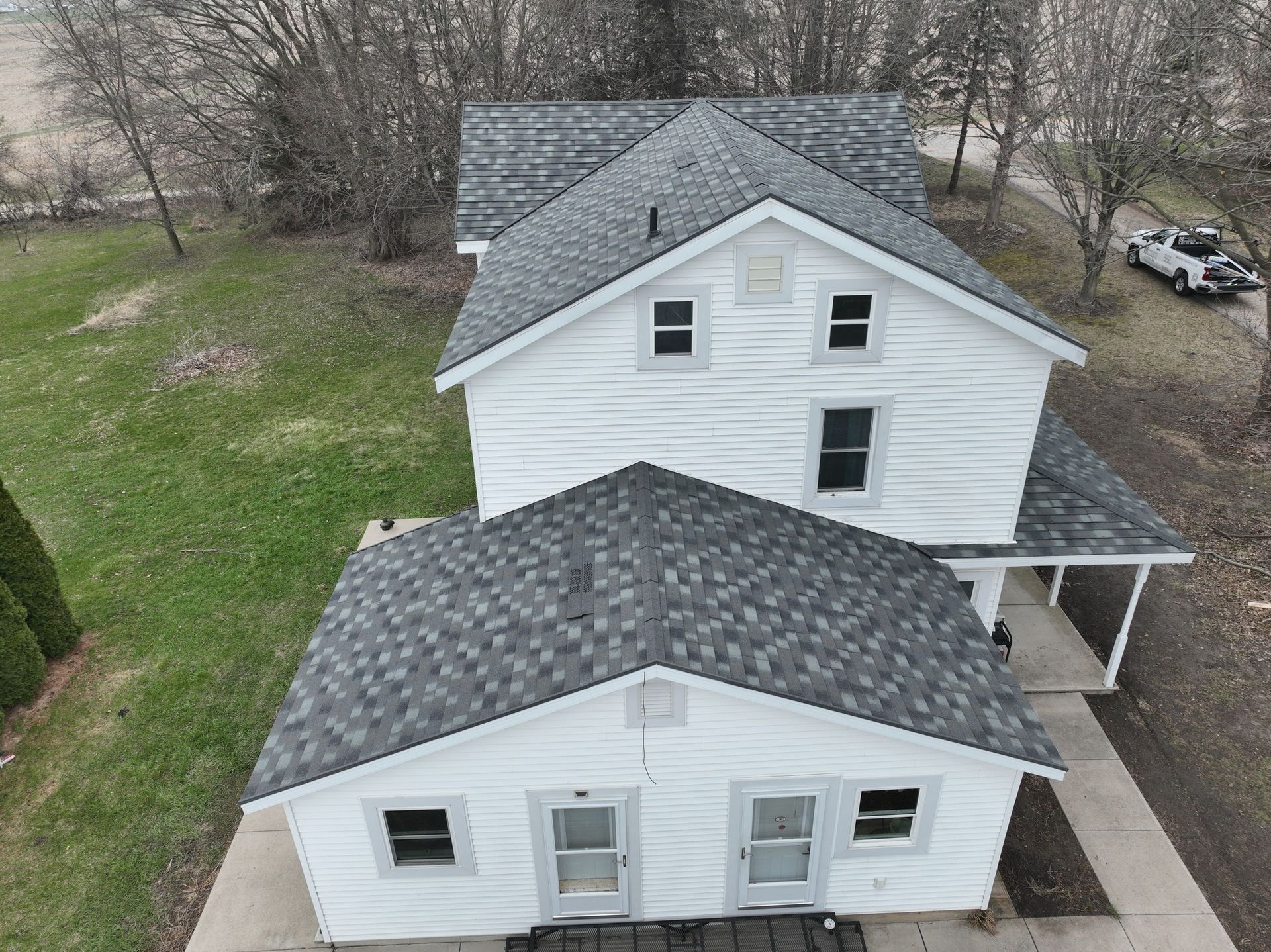 White two-story house with gray shingle roof and attached one-story building, viewed from above.