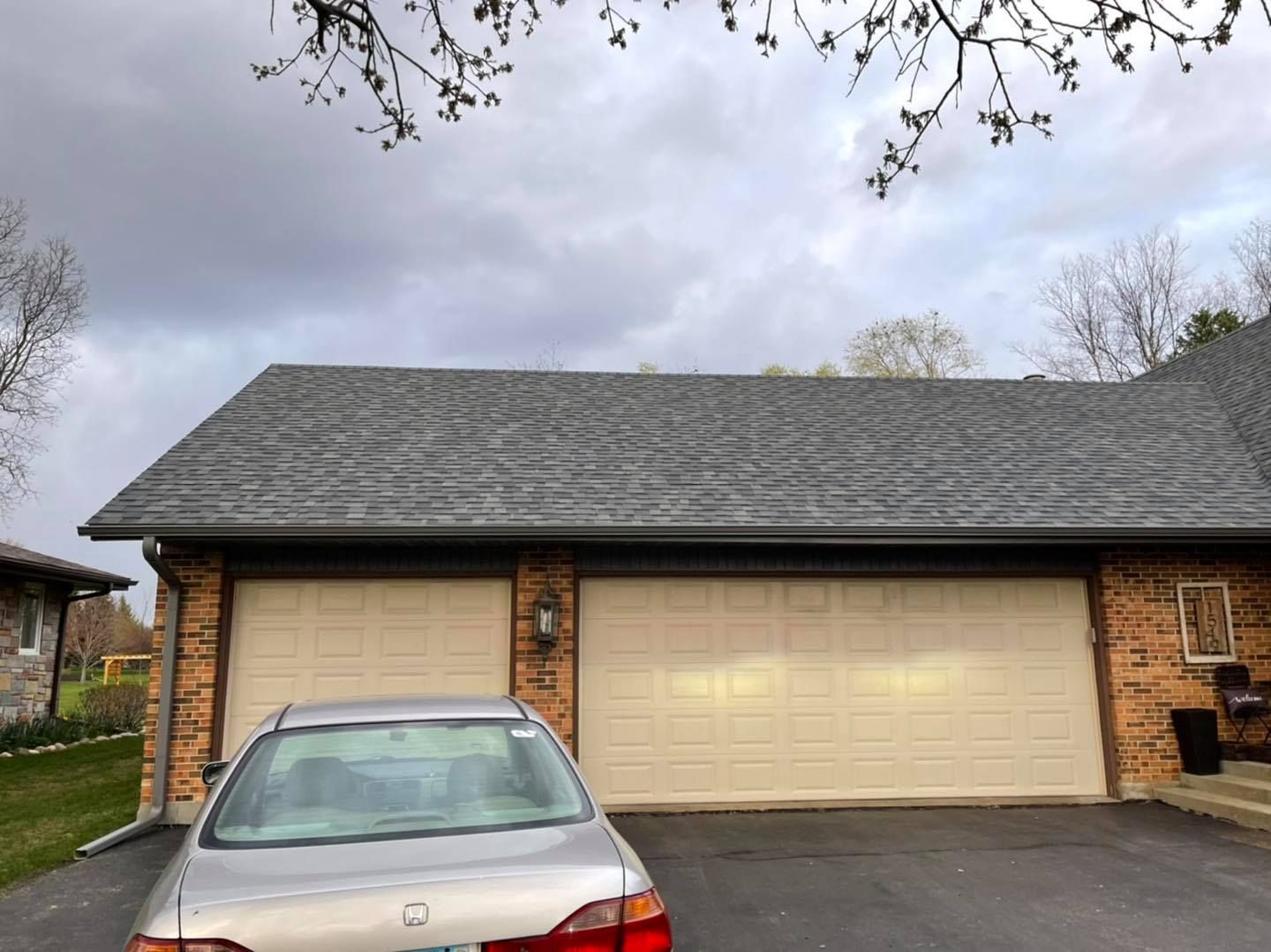 Silver car parked in front of a two-car garage with a gray roof and brick exterior on a cloudy day.