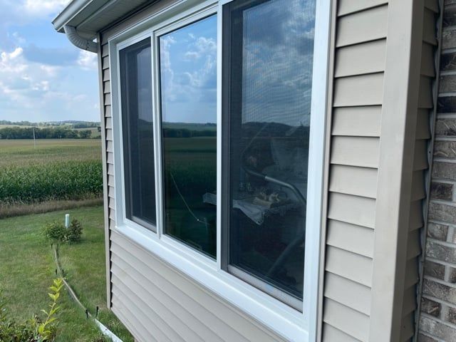 Exterior view of a house with a window, beige siding, and a rural landscape backdrop.