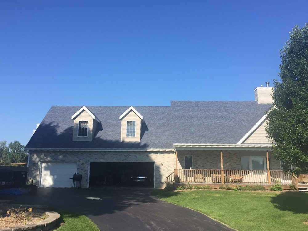 A two-story house with a garage, porch, and dormers under a blue sky.