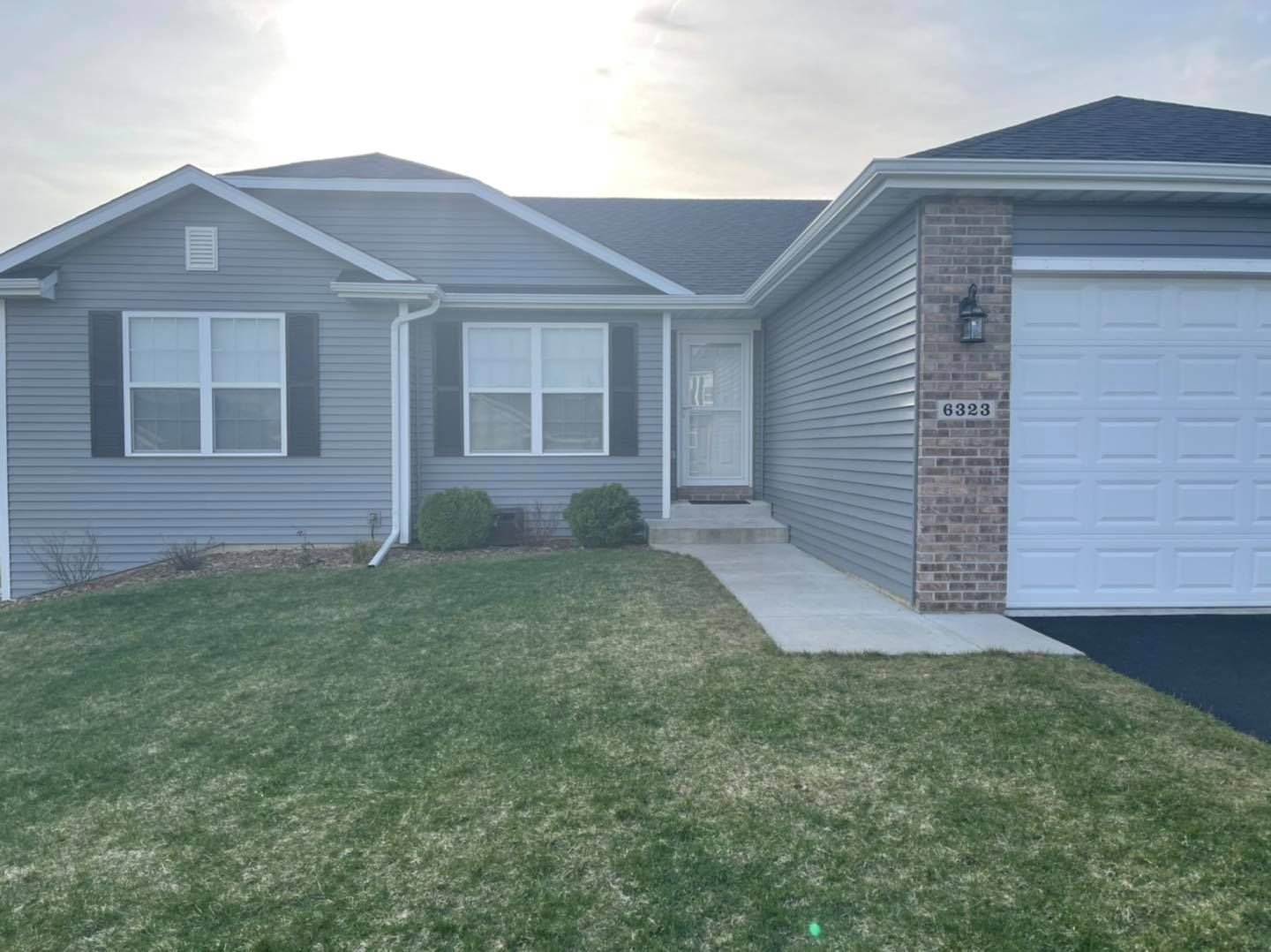 A gray house with black shutters and a brick accent next to a two-car garage on a green lawn.