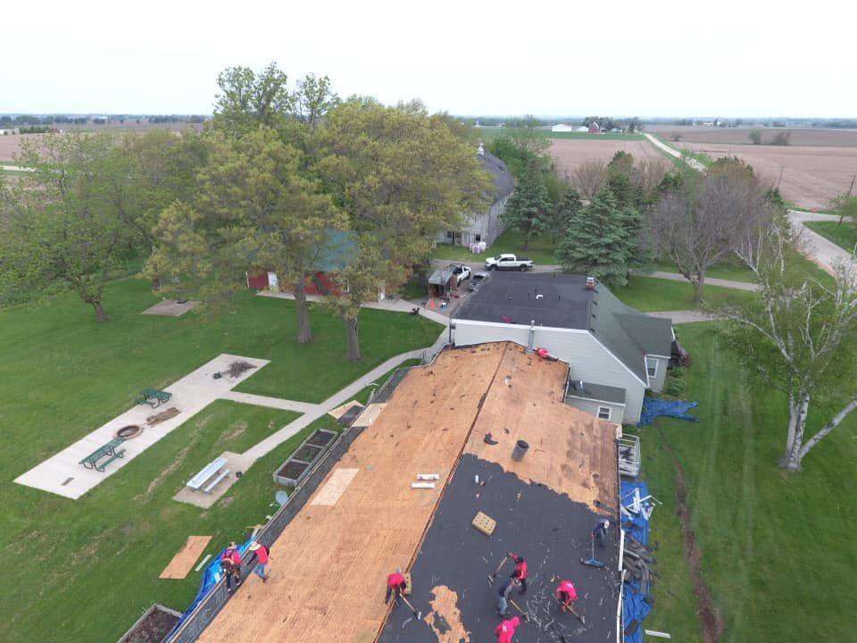 Roofers in red shirts working on a roof replacement in a rural setting.