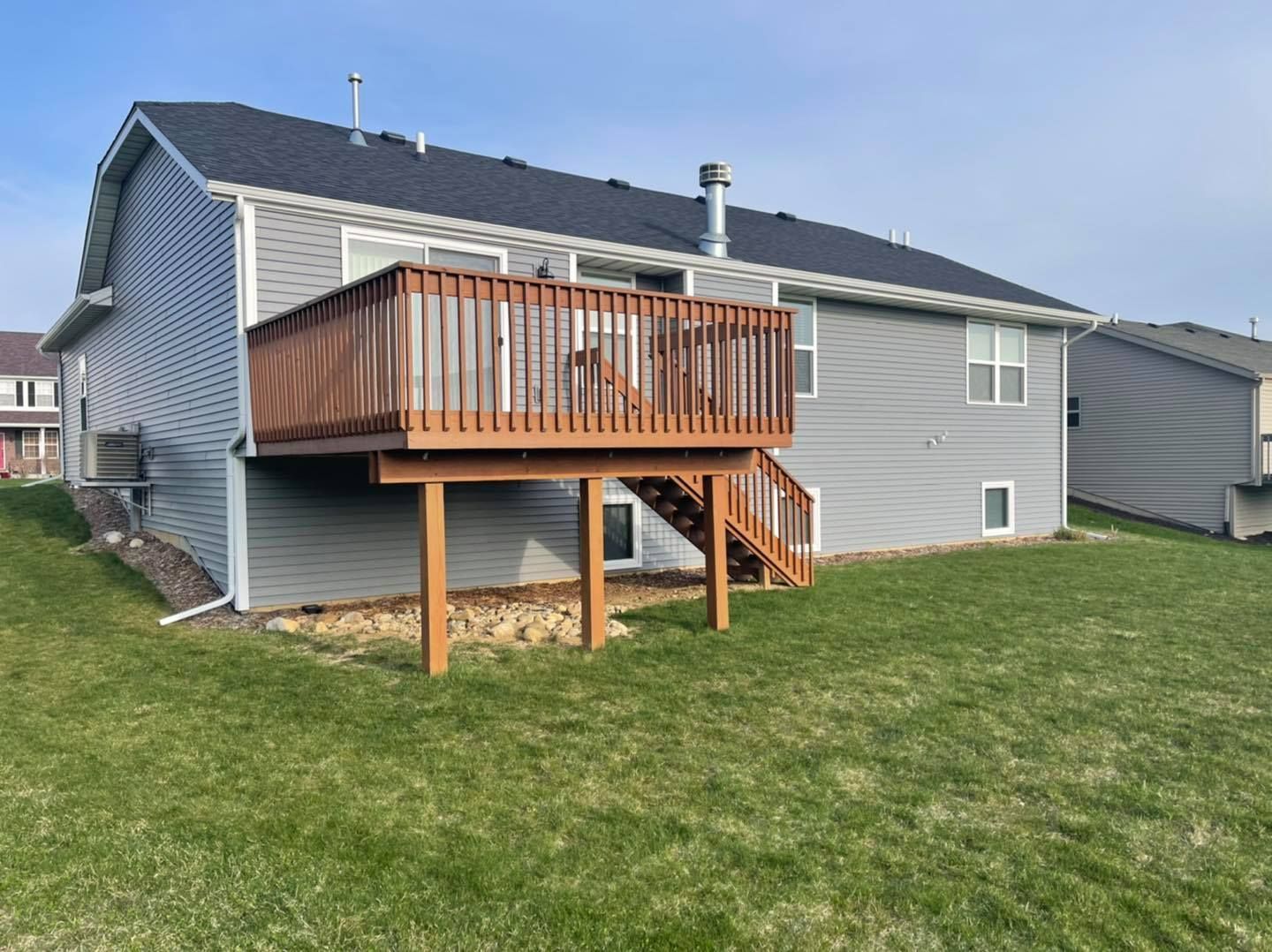 Backyard deck with wooden railing on a gray house, brown steps to the ground, green grass.