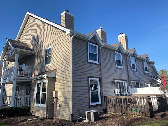 Multi-story beige townhouses with white trim, a deck, and a blue sky.