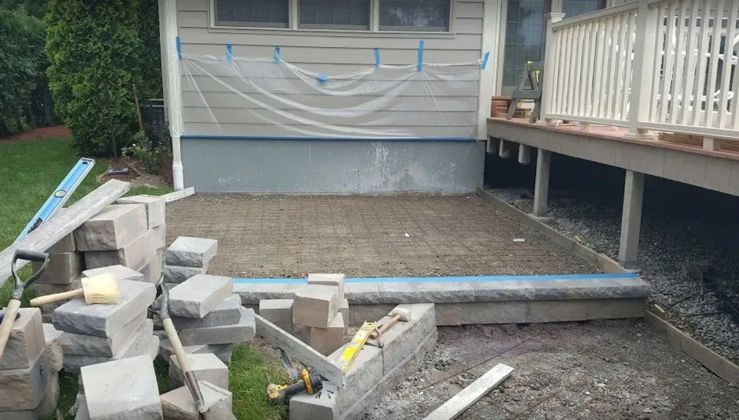 Patio construction: Bricks, gravel base, building materials, and a house with a deck.