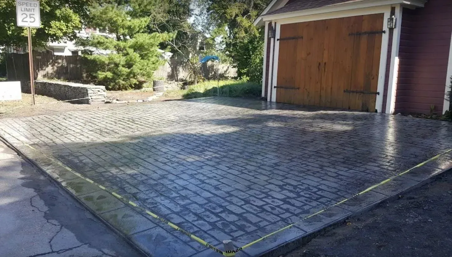A stamped concrete driveway in front of a wooden garage with a speed limit sign in the background.