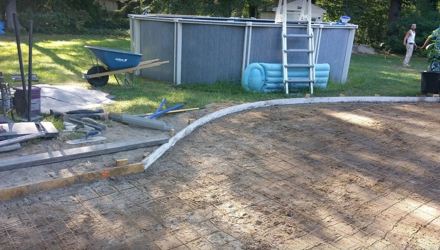 A backyard with an above-ground pool, a concrete area being constructed, and a person in the background.