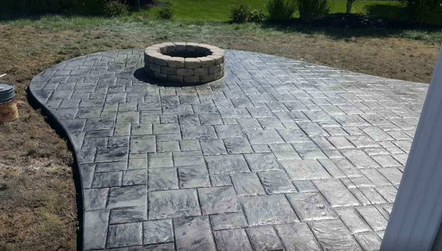 Stamped concrete patio with fire pit, grey color, in a grassy backyard setting.