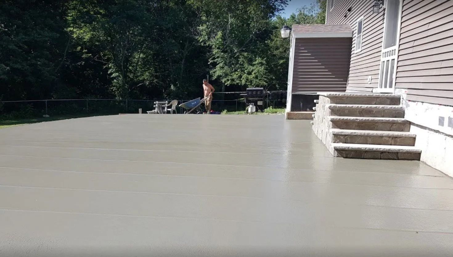 A newly poured concrete patio, adjacent to a house, with steps leading up to a door.