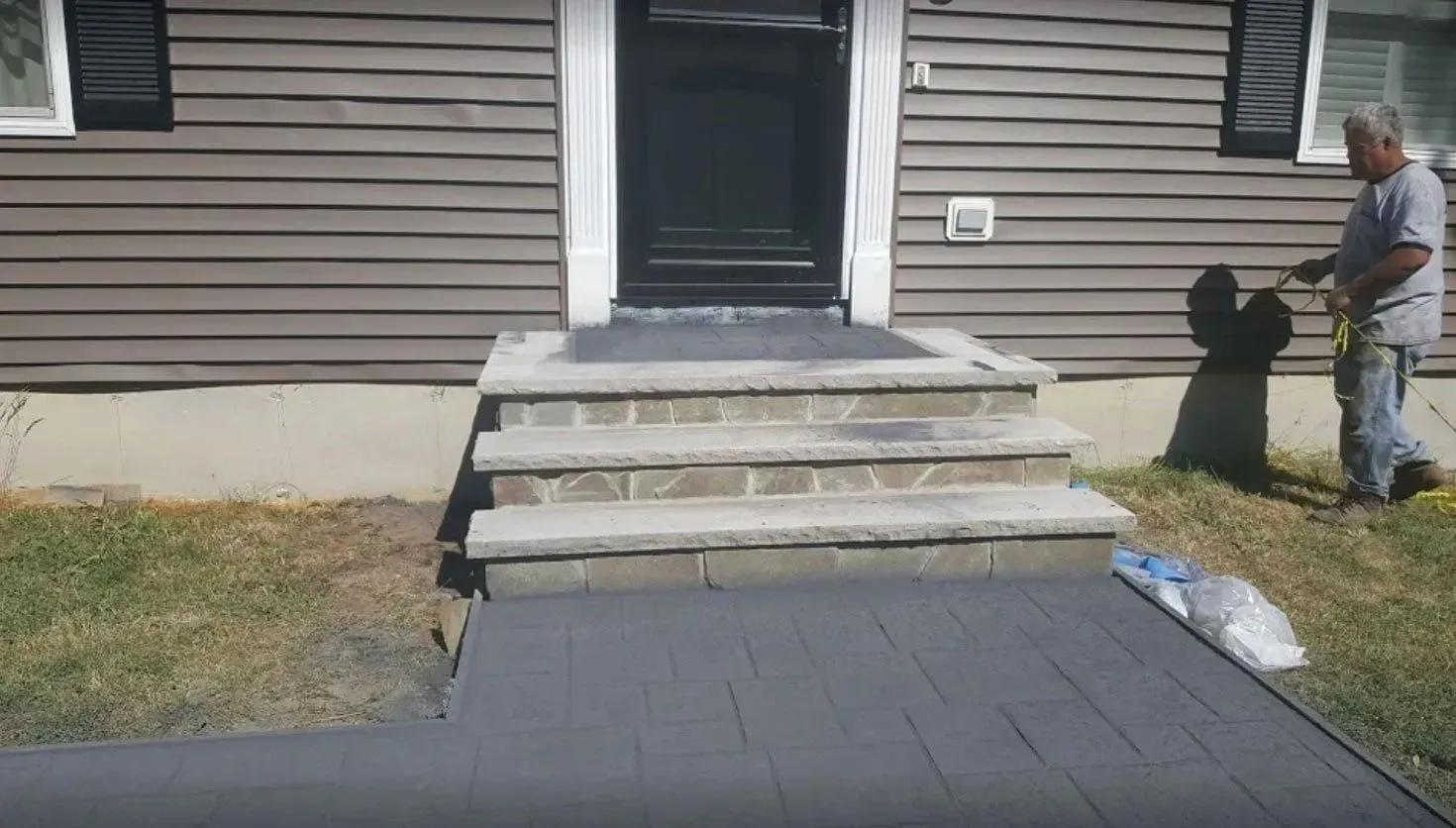 Man painting exterior concrete steps and walkway of a house charcoal grey.