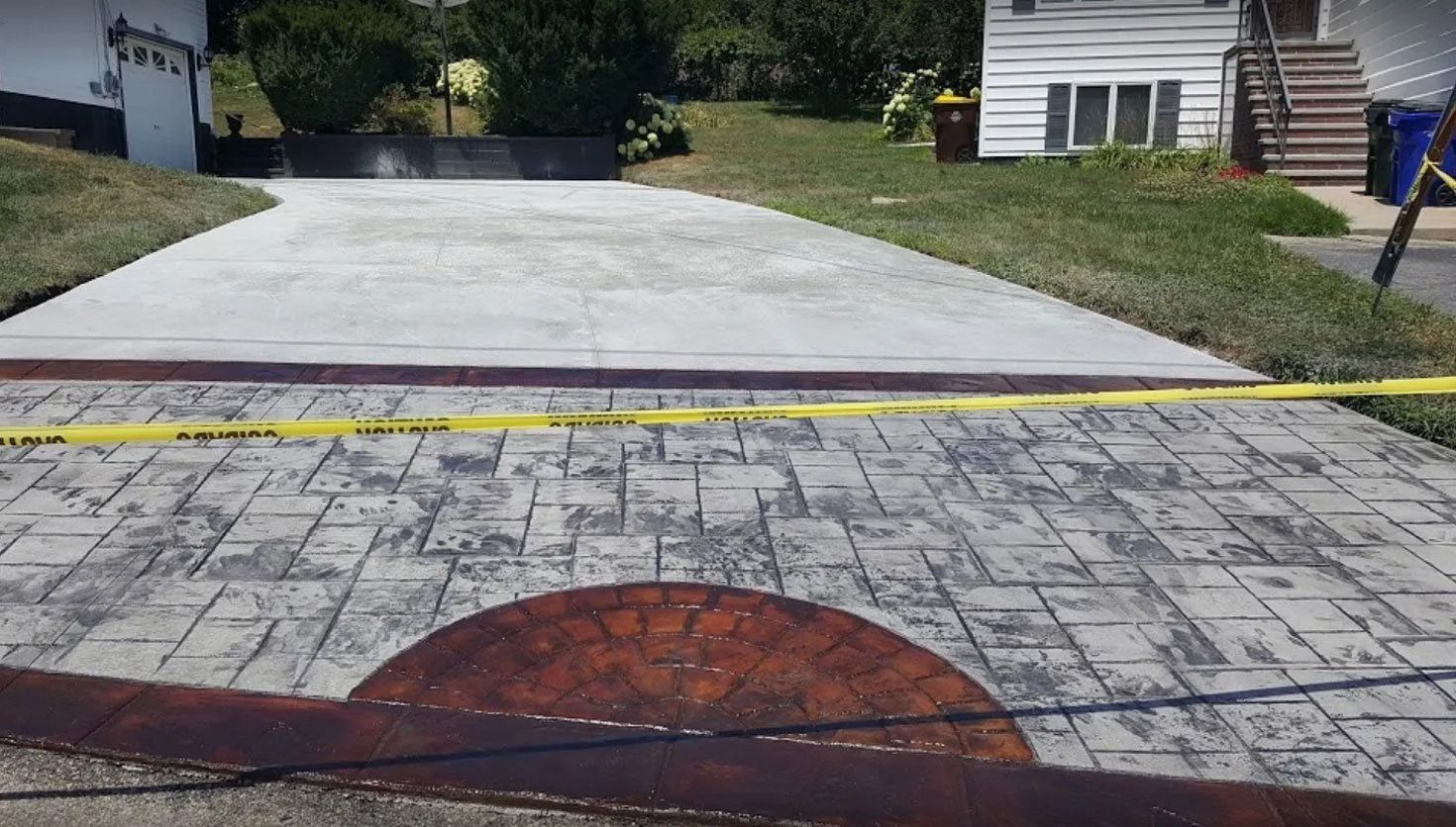 Driveway with a patterned concrete lower section, and a smooth concrete upper section, separated by caution tape.