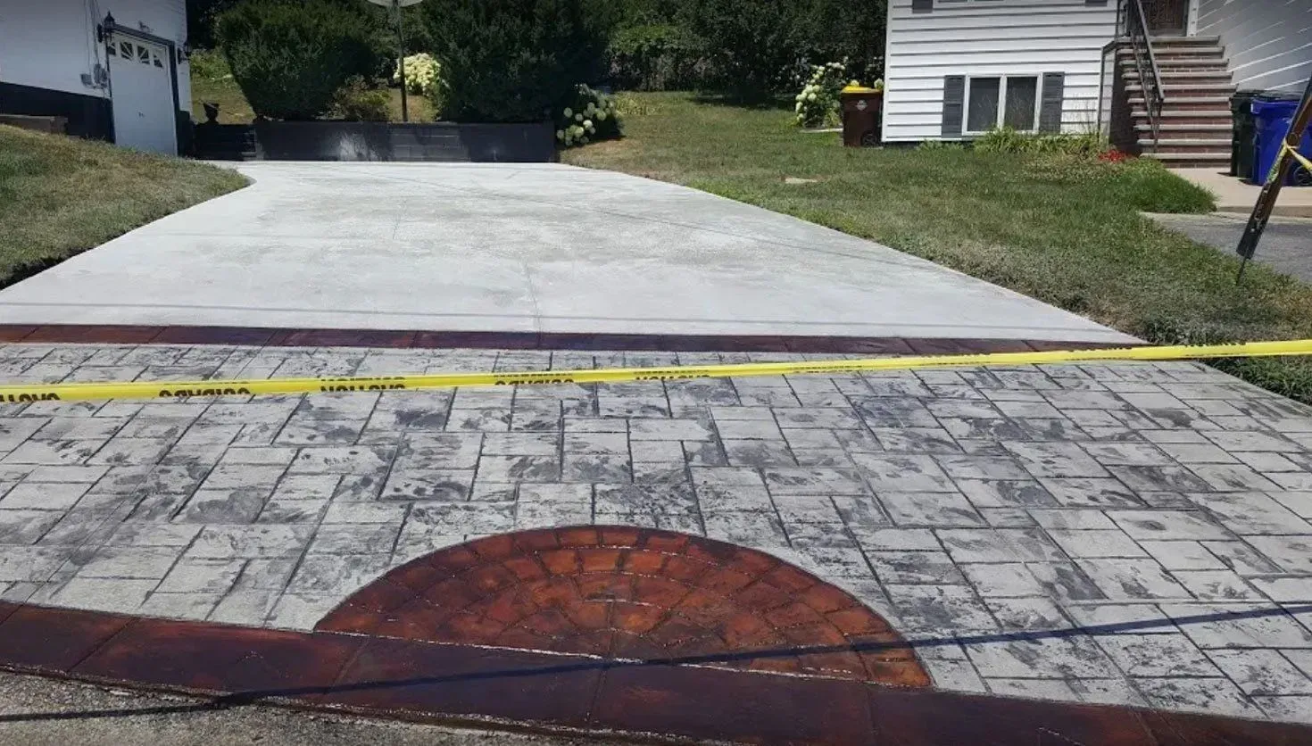 Driveway with new decorative stamped concrete and plain concrete leading to a house.