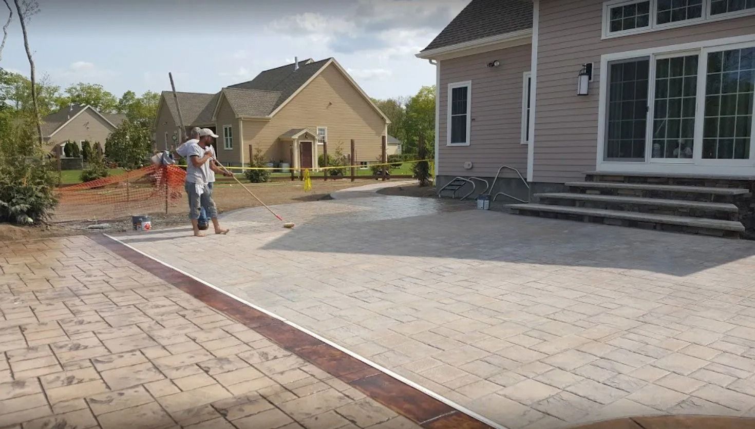 A person working on a brick patio, with a house in the background.