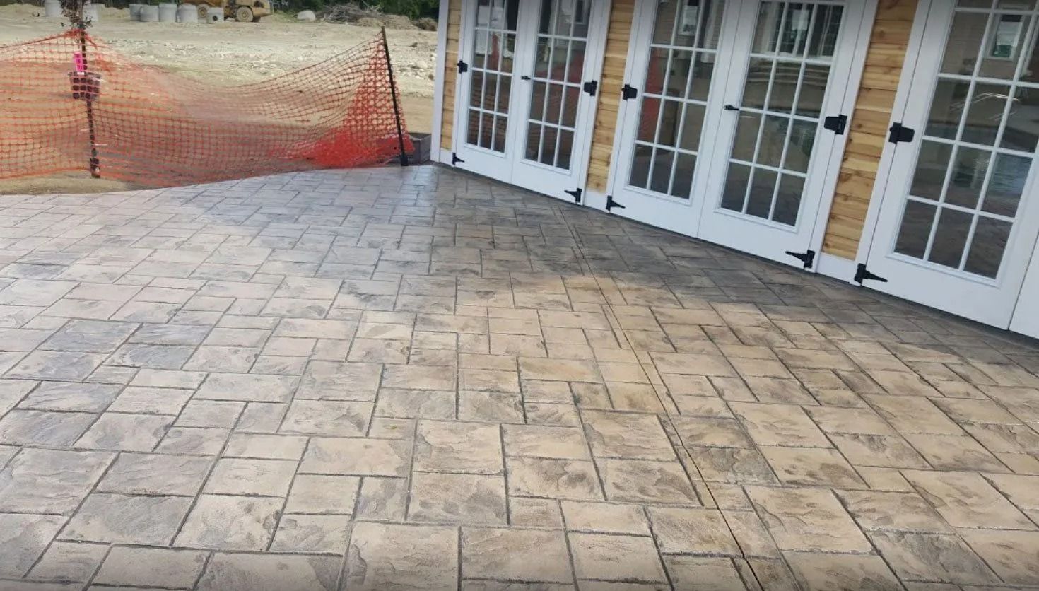 Stamped concrete patio with brick pattern, tan and gray, next to a building with white French doors.