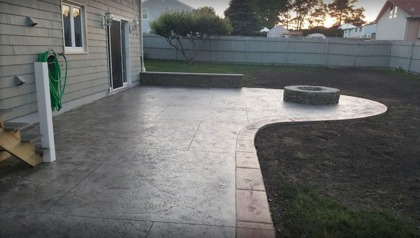 Concrete patio with fire pit and a house in the background, gray and brown colors.