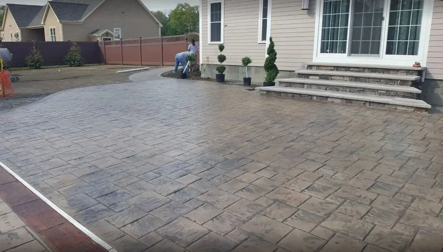 Stamped concrete patio with brick border, steps, and a person walking in the background.
