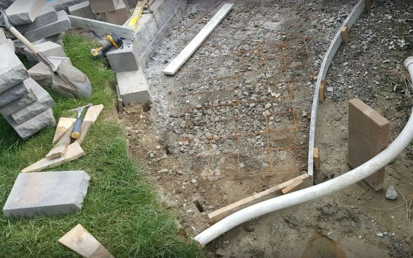 Construction site with stone blocks, gravel, and a white pipe on a grassy area.