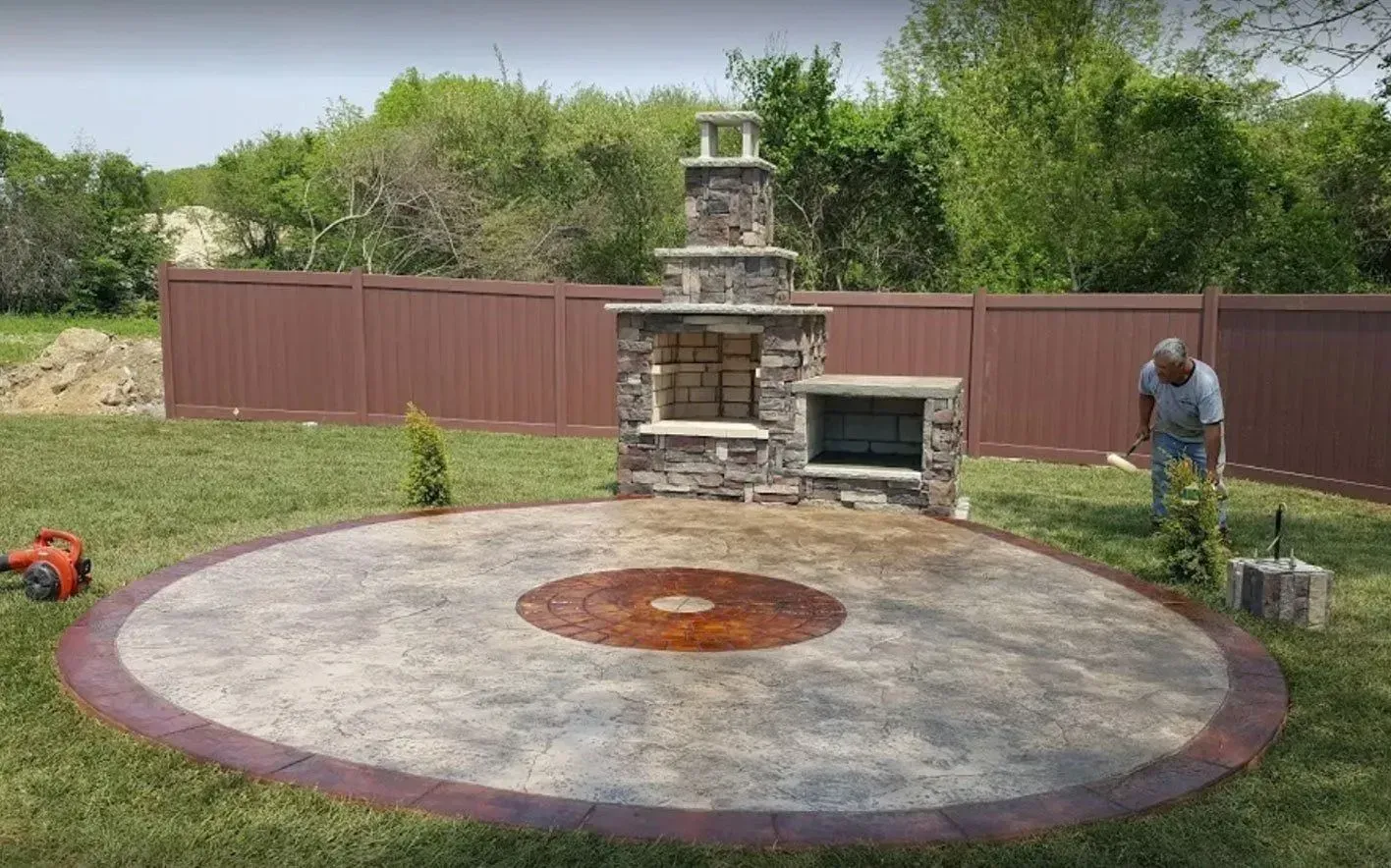 Outdoor patio with a stone fireplace and grill; a person is planting a bush.