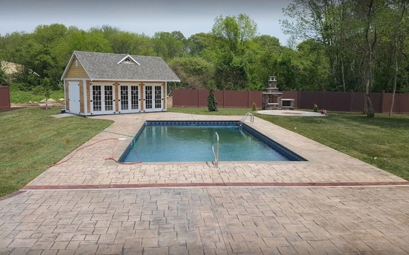 Swimming pool with brick patio, yellow pool house, and outdoor fireplace.