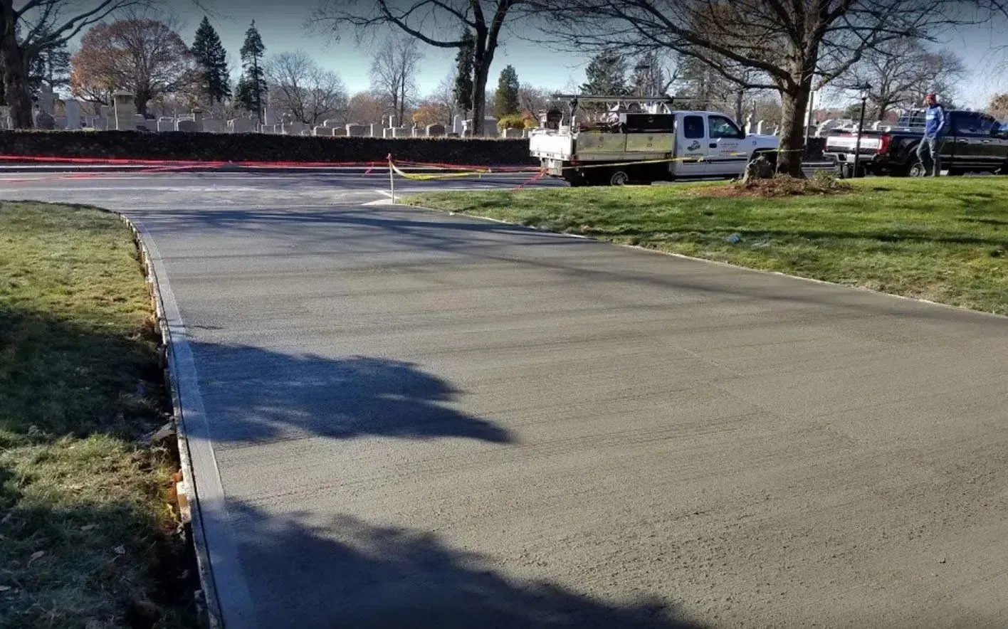 New concrete pathway in a cemetery, with work vehicles and green grass on a sunny day.