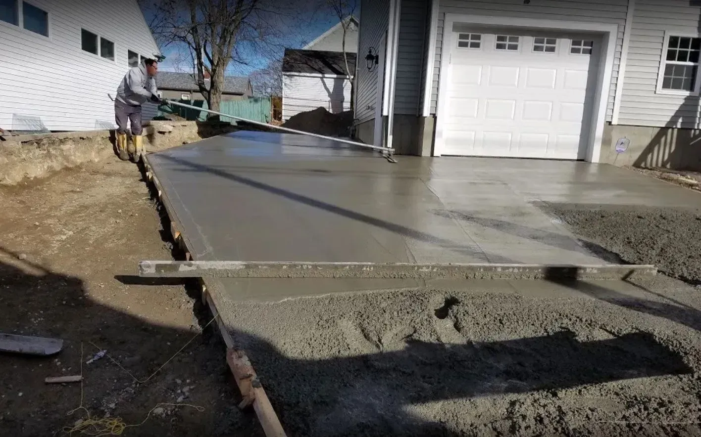 Person smoothing wet concrete driveway with a level near a garage on a sunny day.