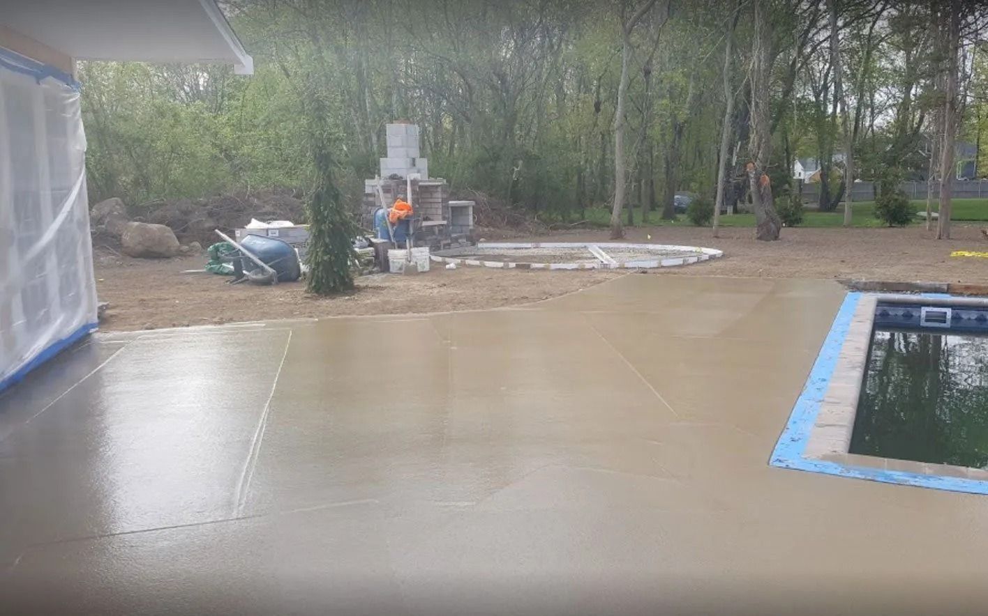 Backyard with wet concrete patio, pool, and outdoor fireplace; construction in progress.